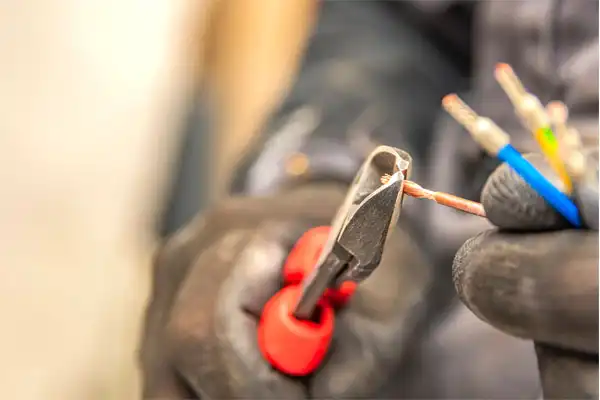 Gloved hands using wire cutters to strip electrical wires with exposed copper.