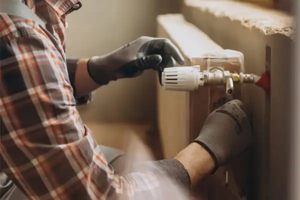Person in checkered shirt and gloves adjusting a valve on a radiator.