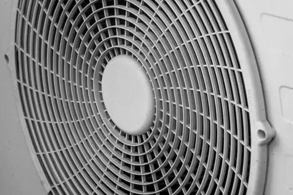 Close-up of a circular fan grill with a central hub, featuring a pattern of concentric rings and intersecting lines in a light-colored material.