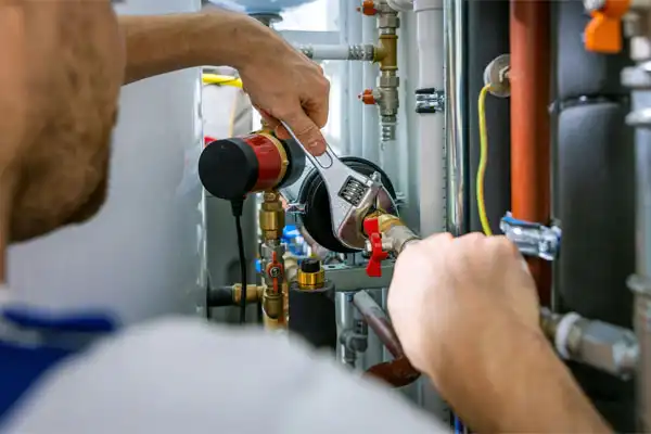 Person using a wrench to tighten a pipe in a plumbing setup with various pipes and valves in the background.