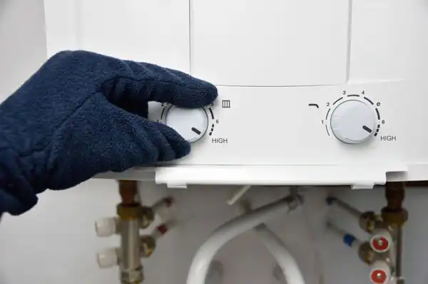 A gloved hand adjusts the temperature dial on a water heater, indicating a high setting.