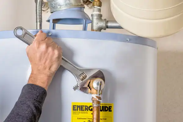 A person's hand holds a wrench, tightening a pipe connection on a water heater.