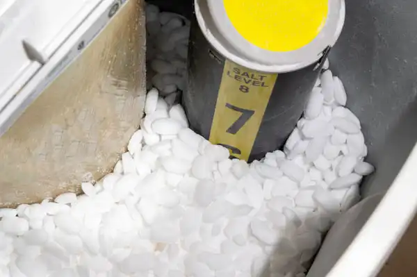 Close-up of a water softener with a salt level indicator showing level 7. The surrounding area is filled with coarse salt pellets.
