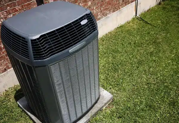 Outdoor air conditioning unit on a concrete pad next to a brick wall, surrounded by grass.