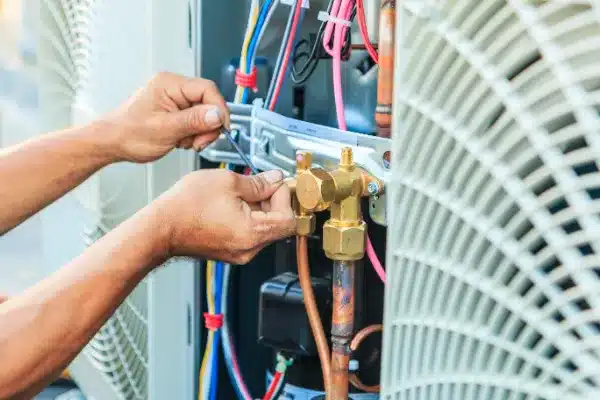 Hands using a wrench to adjust wires and components in an air conditioning unit.